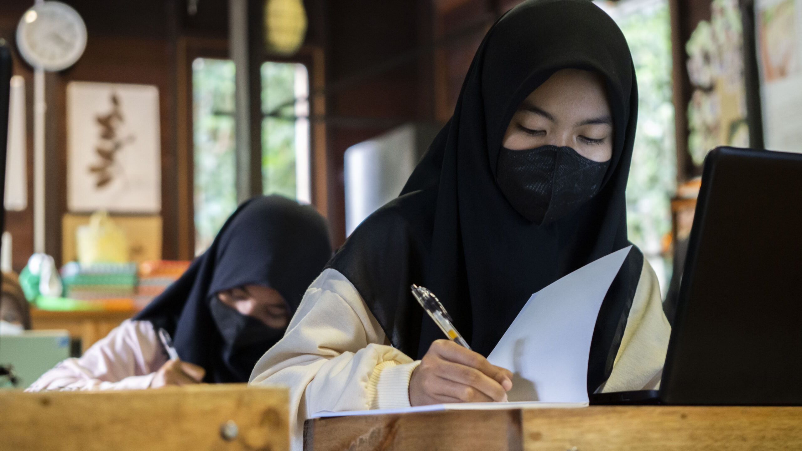 Young female students wearing headscarves in a classroom.